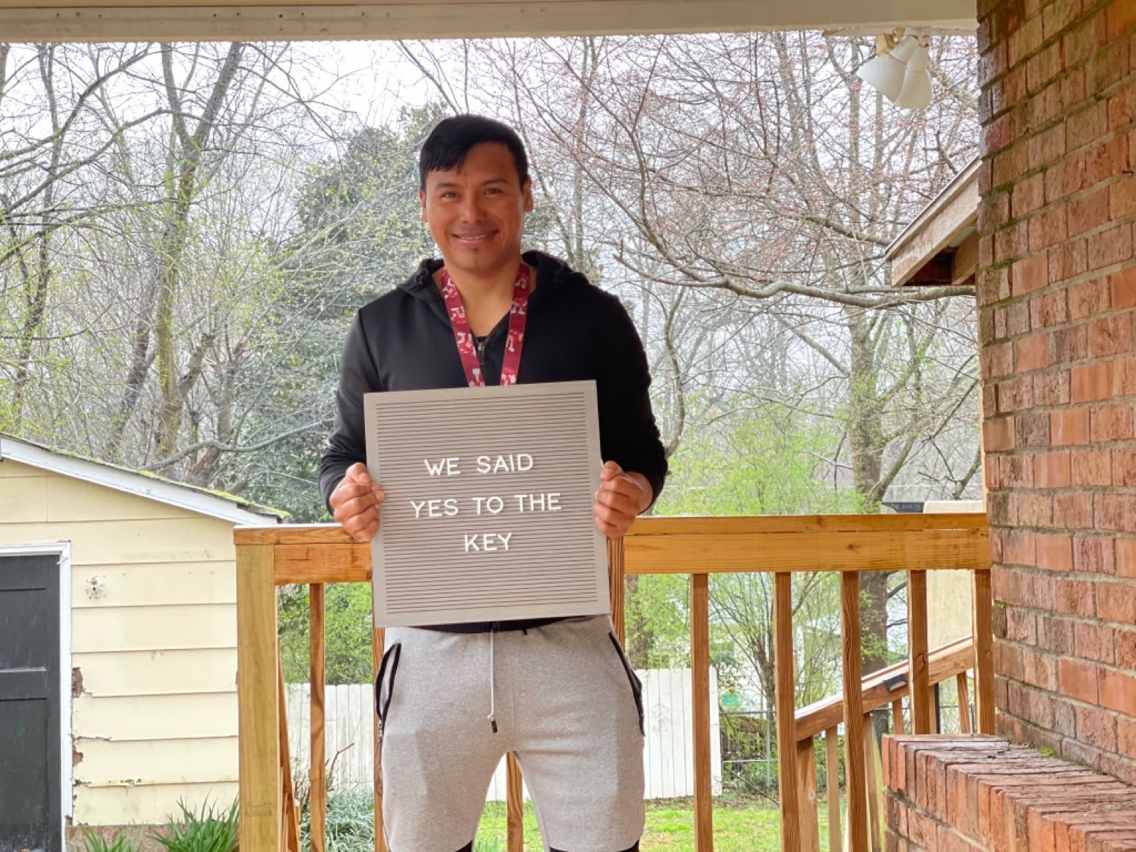 Client holding 'We Said Yes to the Key' sign on their new home porch