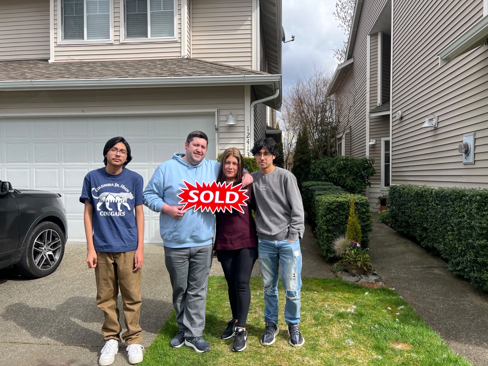 Family celebrating with SOLD sign in front of their new home