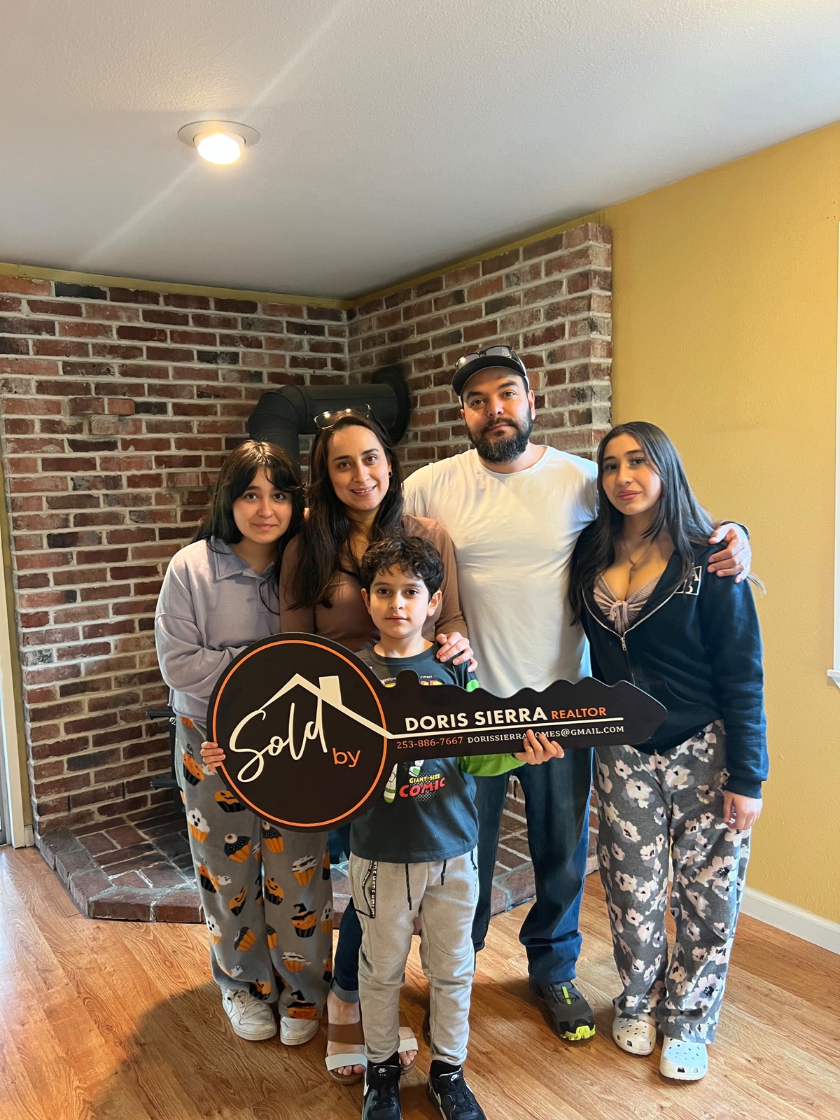 Family holding Sold by Doris Sierra Realtor sign inside their new home