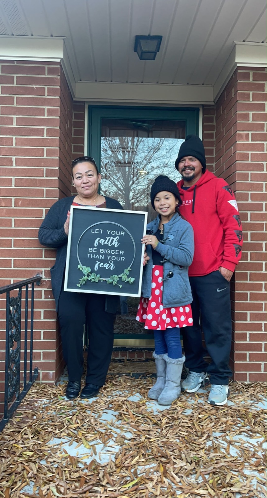 Family of three on the porch of their new brick home holding a celebratory sign